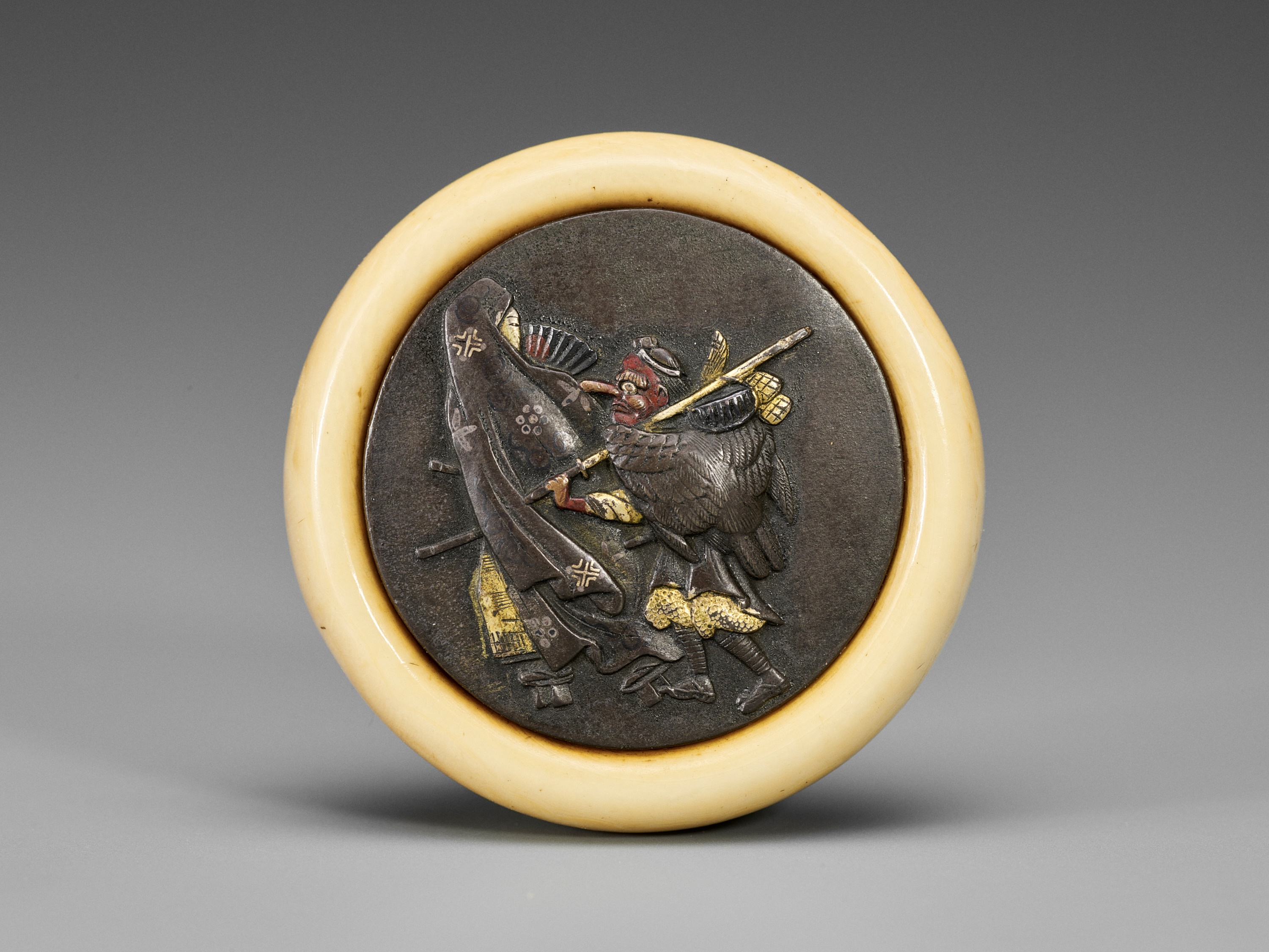 Lot 180 - AN IVORY AND METAL KAGAMIBUTA NETSUKE