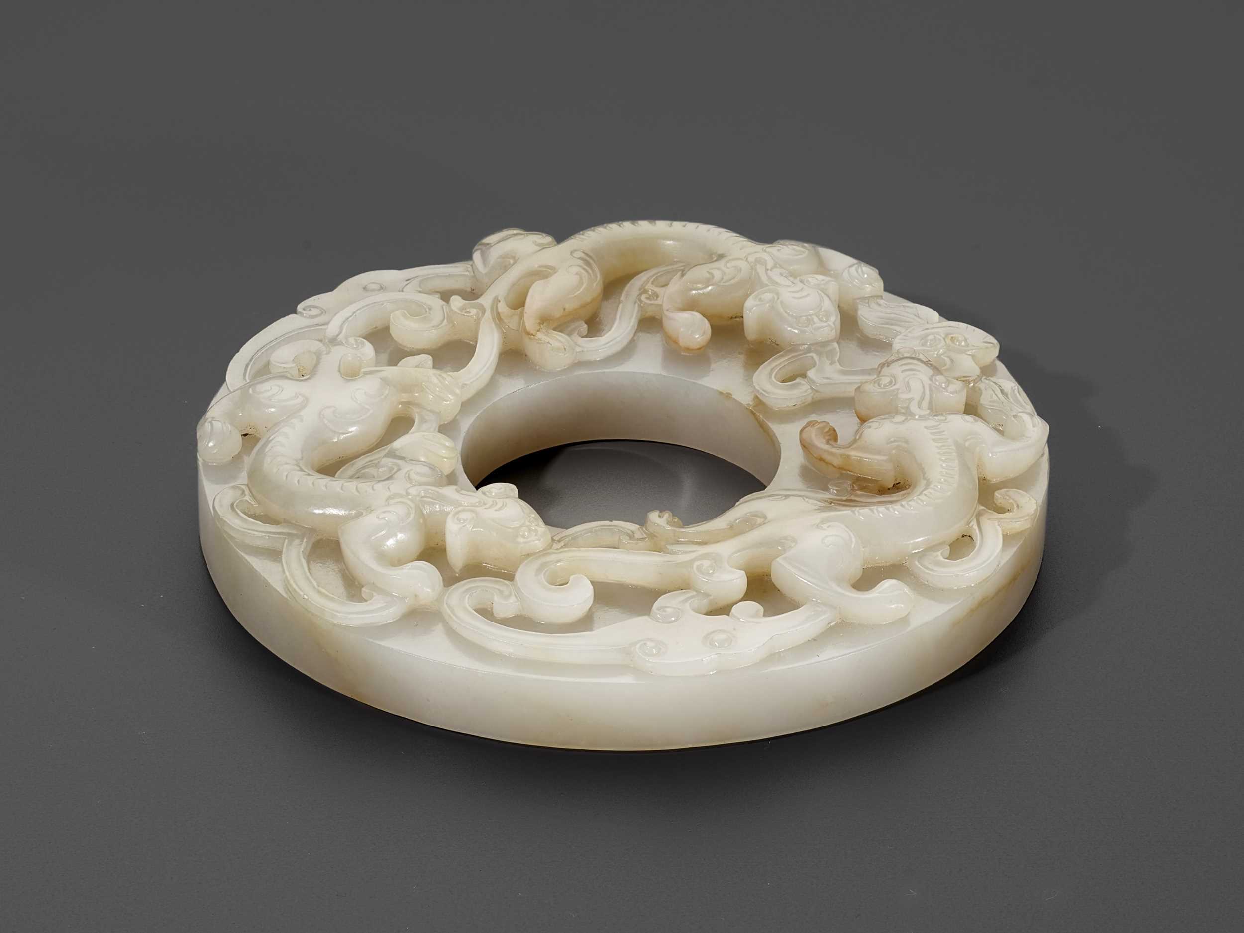 Lot 350 - A PALE CELADON AND RUSSET JADE ‘CHILONG’ DISC, BI, QING DYNASTY