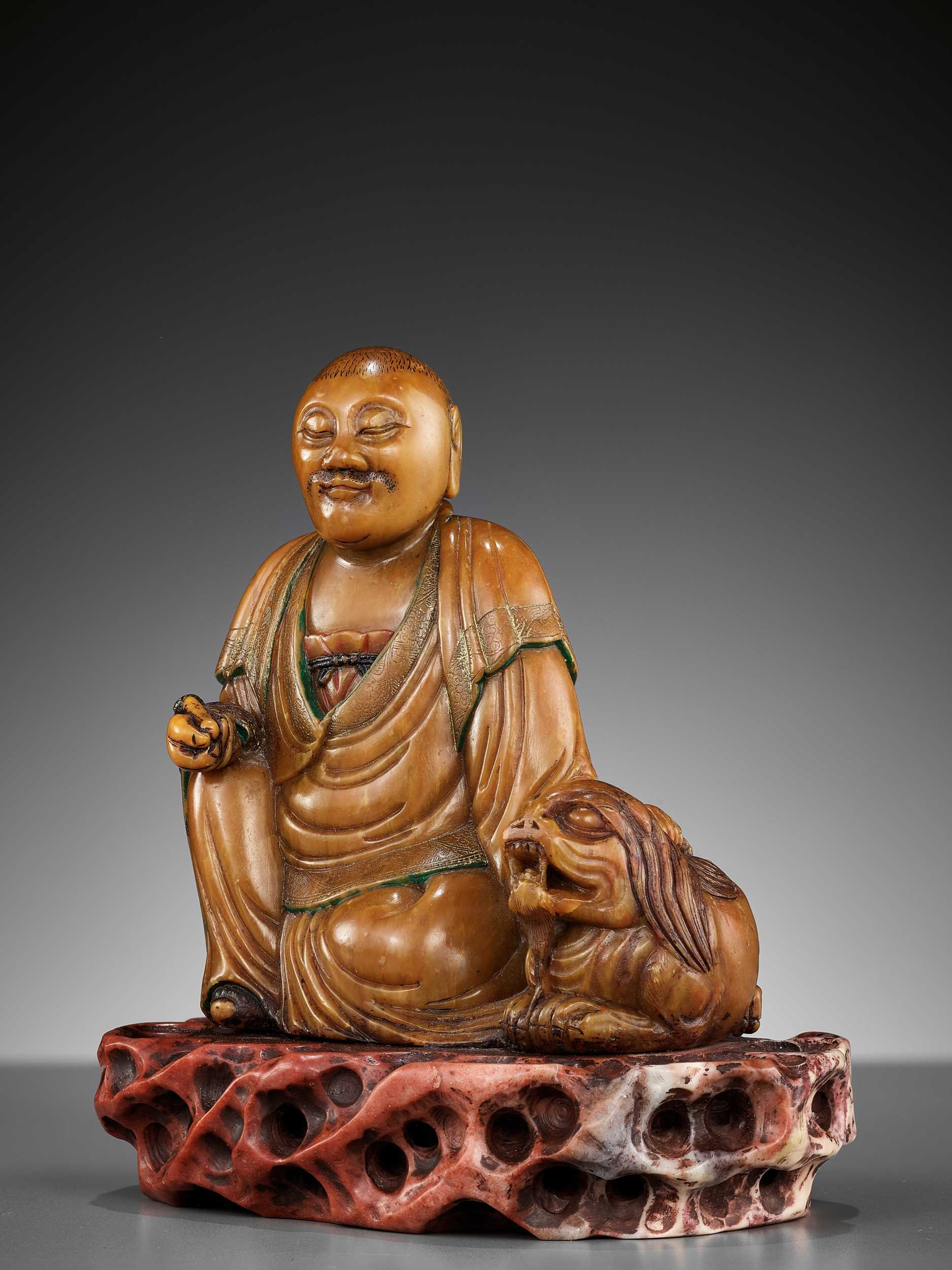 Lot 27 - A SOAPSTONE FIGURE OF A LUOHAN WITH A BUDDHIST LION, 18TH CENTURY