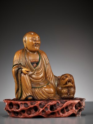Lot 27 - A SOAPSTONE FIGURE OF A LUOHAN WITH A BUDDHIST LION, 18TH CENTURY