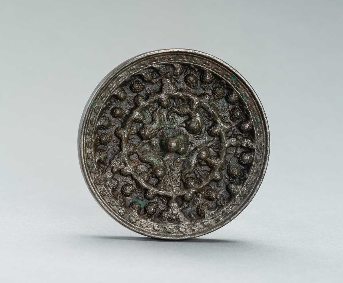 Lot 228 - A SILVERY TANG DYNASTY BRONZE ‘LION AND GRAPEVINE’ MIRROR