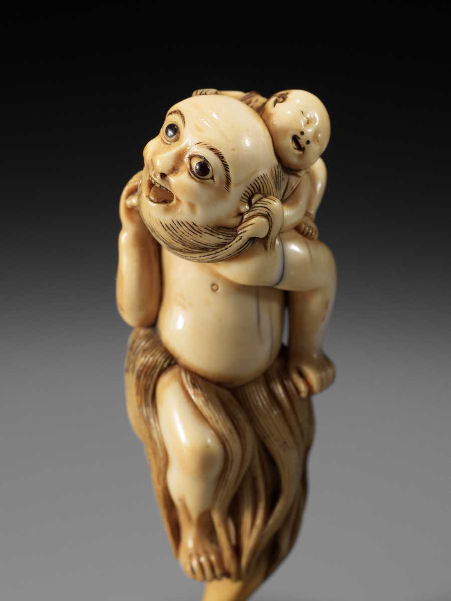 Lot 21 - A SUPERB IVORY NETSUKE OF A FISHERMAN CARRYING A BOY, ATTRIBUTED TO GECHU