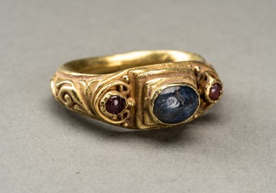 Lot 631 - A GANDHARAN GOLD RING INLAID WITH SAPPHIRE AND TWO SMALL GARNETS