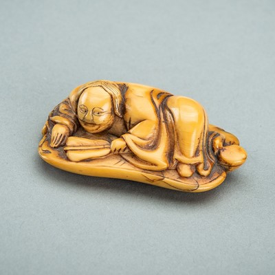 Lot 1268 - AN IVORY NETSUKE OF A MAN ON AN UCHIWA (FAN), EDO