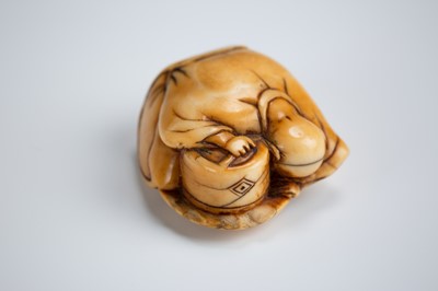 Lot 392 - AN OLD IVORY NETSUKE OF A TEA GRINDER NAPPING BESIDE A MILLSTONE