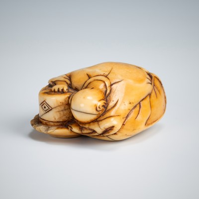 Lot 392 - AN OLD IVORY NETSUKE OF A TEA GRINDER NAPPING BESIDE A MILLSTONE