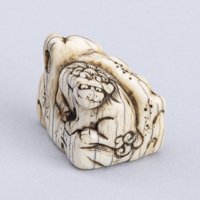 Lot 1300 - AN OLD IVORY NETSUKE OF A SHISHI ON A ROCK, 18TH CENTURY