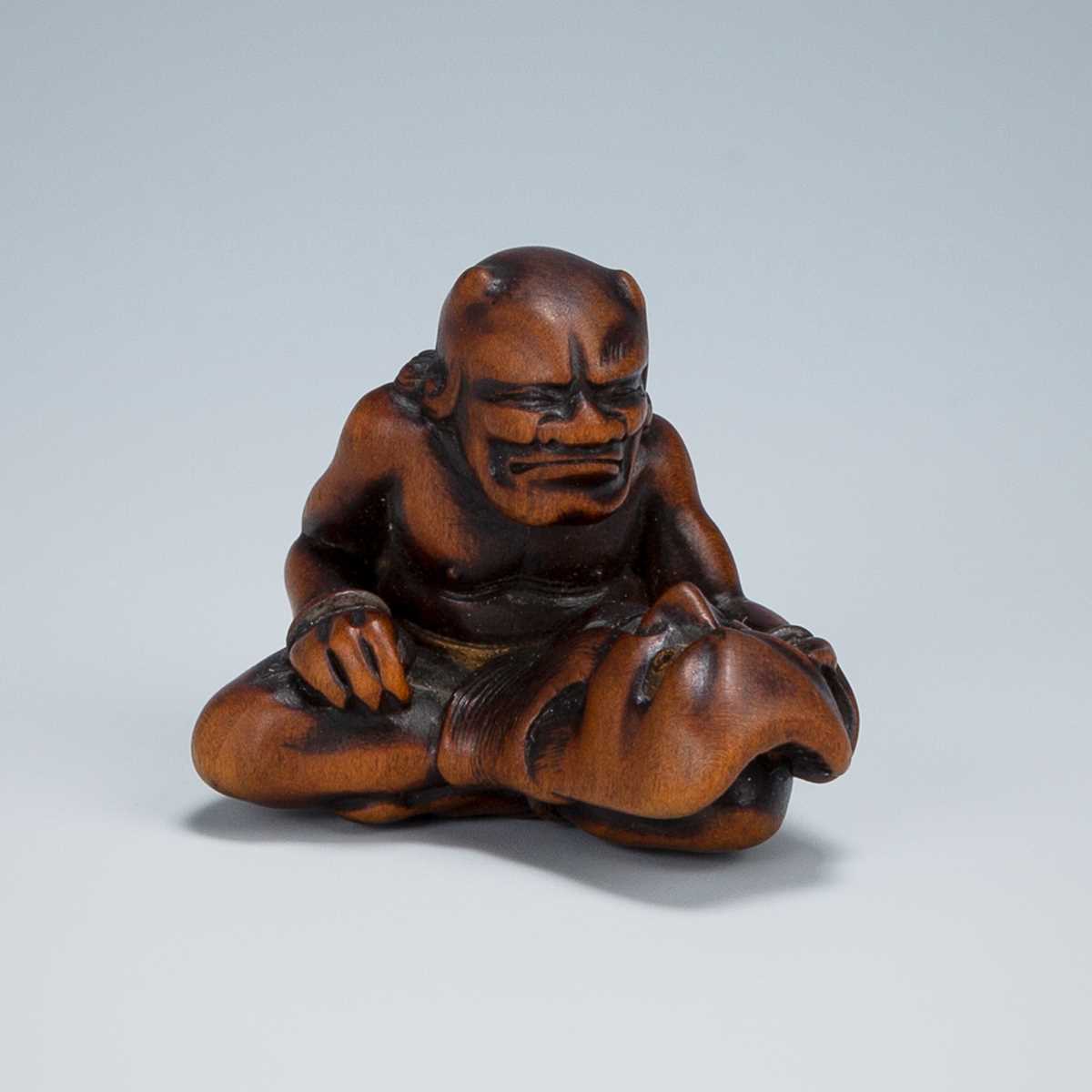 Lot 389 - GYOKKEI: A WOOD NETSUKE OF AN ONI INSPECTING A SHOKI MASK