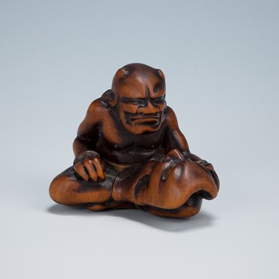 Lot 389 - GYOKKEI: A WOOD NETSUKE OF AN ONI INSPECTING A SHOKI MASK