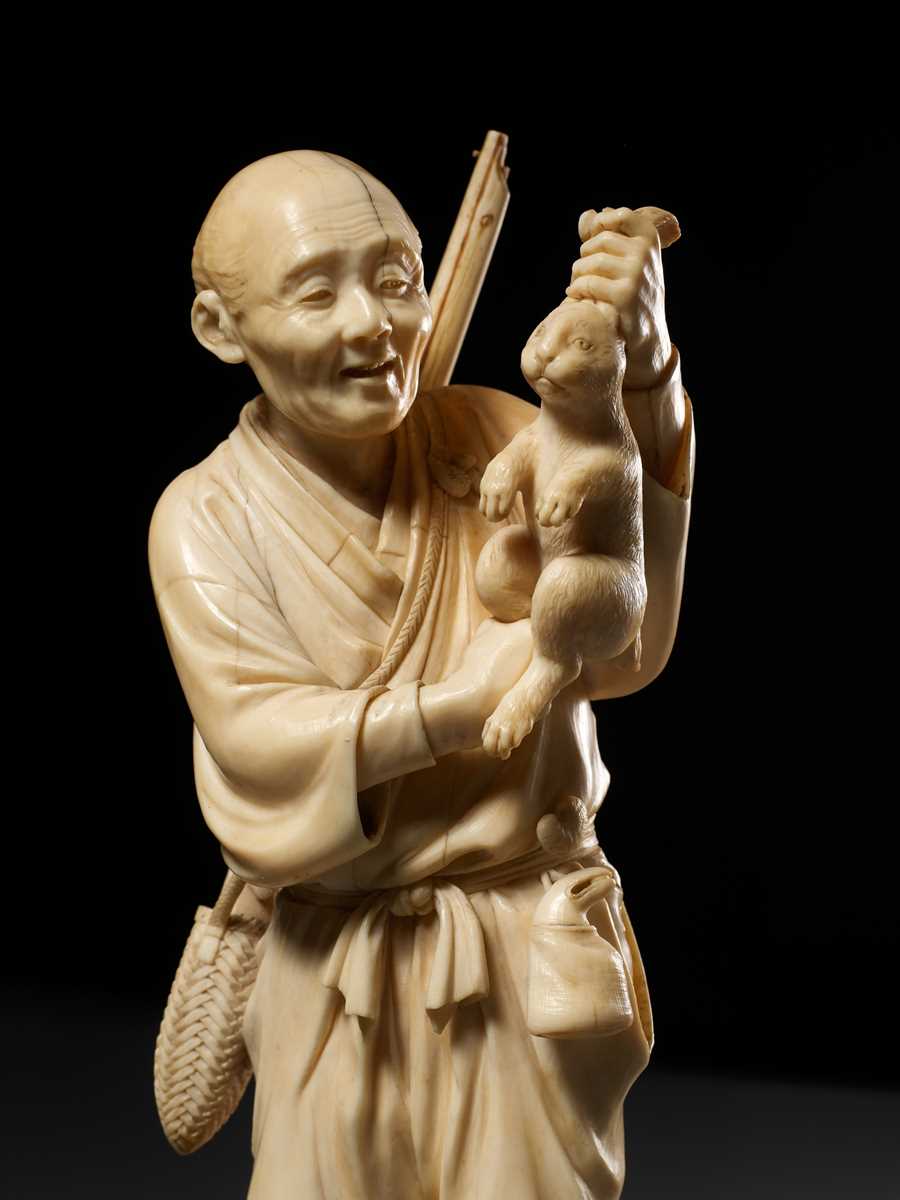 Lot 138 - KOSEI: A FINE TOKYO SCHOOL IVORY OKIMONO OF A HUNTER HOLDING A HARE
