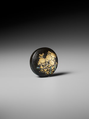 A LACQUERED WOOD MANJU NETSUKE DEPICTING CHRYSANTHEMUMS BY A FENCE