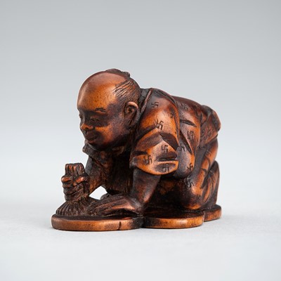 A BOXWOOD NETSUKE OF A MAN POLISHING A CHARACTER