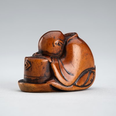 Lot 576 - A FINE WOOD NETSUKE OF A TEA GRINDER NAPPING BESIDE A MILLSTONE