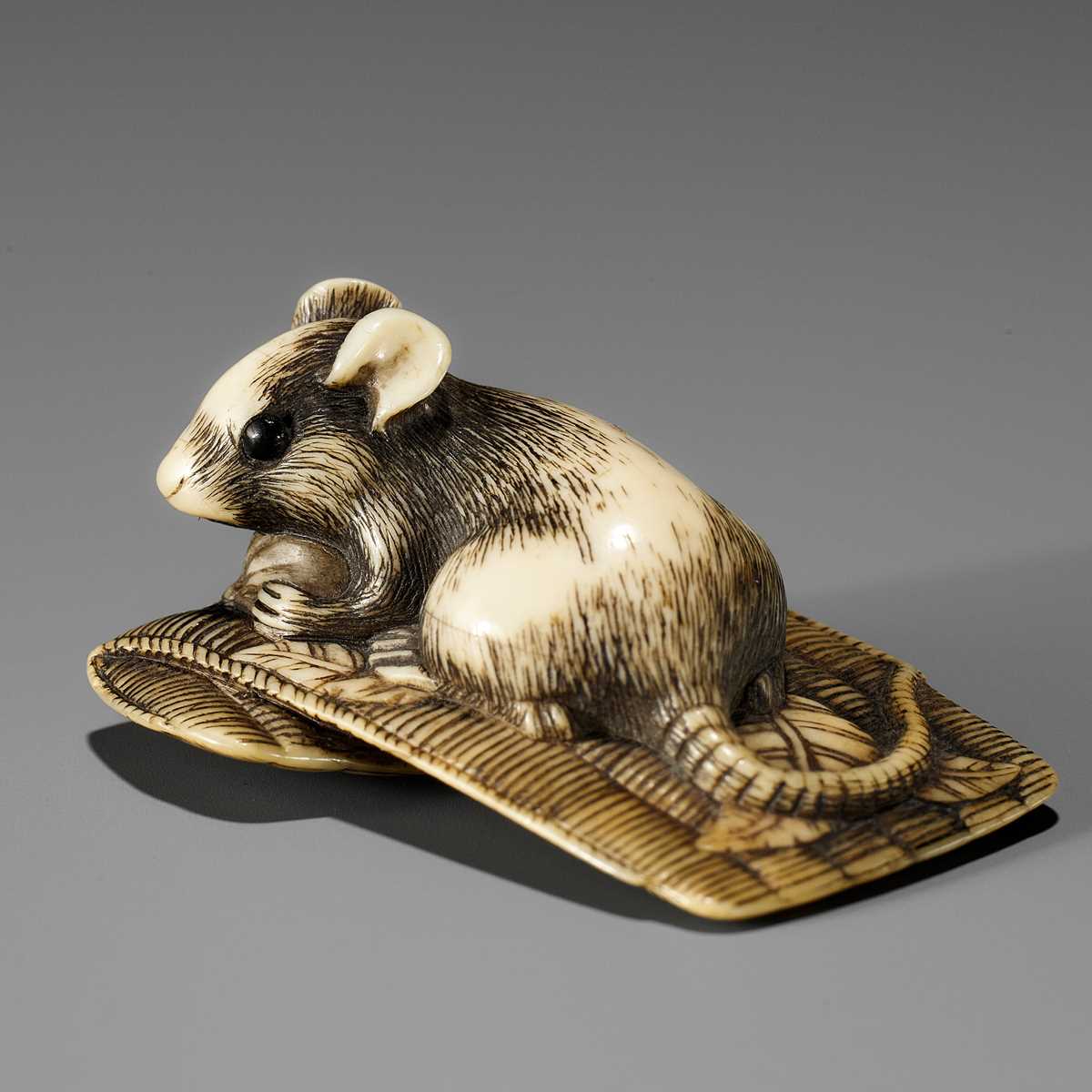 Lot 55 - AN OSAKA SCHOOL IVORY NETSUKE OF A RAT ON A STRAW MAT