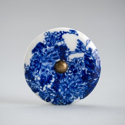 A BLUE AND WHITE PORCELAIN MANJU NETSUKE WITH FLORAL DECORATION