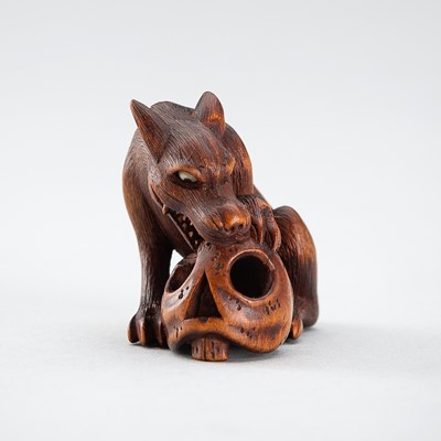 Lot 391 - KAZUSAI: A WOOD NETSUKE OF A WOLF GNAWING ON A SKULL