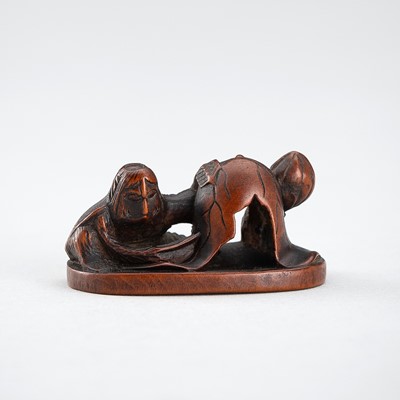 A WOOD NETSUKE OF A KAPPA LOOKING UNDER A LOTUS LEAF