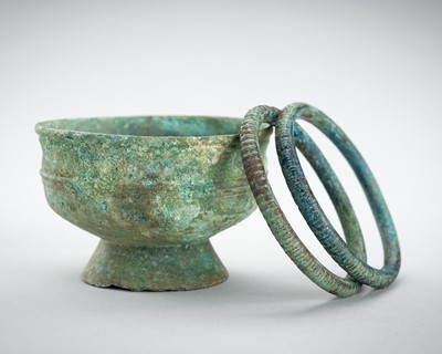 Lot 970 - A BRONZE STEM CUP AND TWO BRACELETS, ANGKOR PERIOD, 10TH-12TH CENTURY