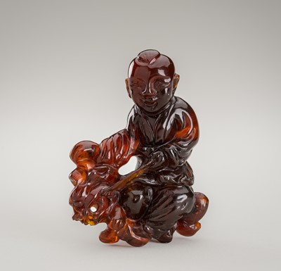 Lot 779 - A SMALL AMBER CARVING OF A BOY WITH SHISHI, LATE QING DYNASTY