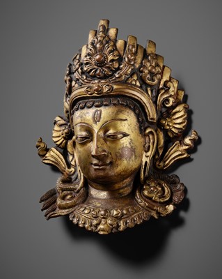 Lot 312 - A GILT-COPPER REPOUSSÉ LINGA COVER WITH THE FACE OF SHIVA, MALLA PERIOD, NEPAL, 15TH-16TH CENTURY