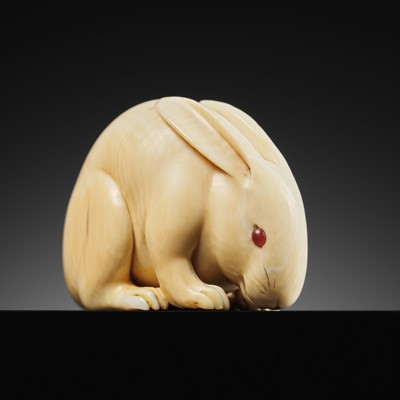 Lot 98 - MASAMITSU: A FINE IVORY NETSUKE OF A HARE WITH AMBER EYES