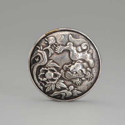 A SILVER AND BRONZE KAGAMIBUTA NETSUKE WITH A SHISHI AND PEONIES