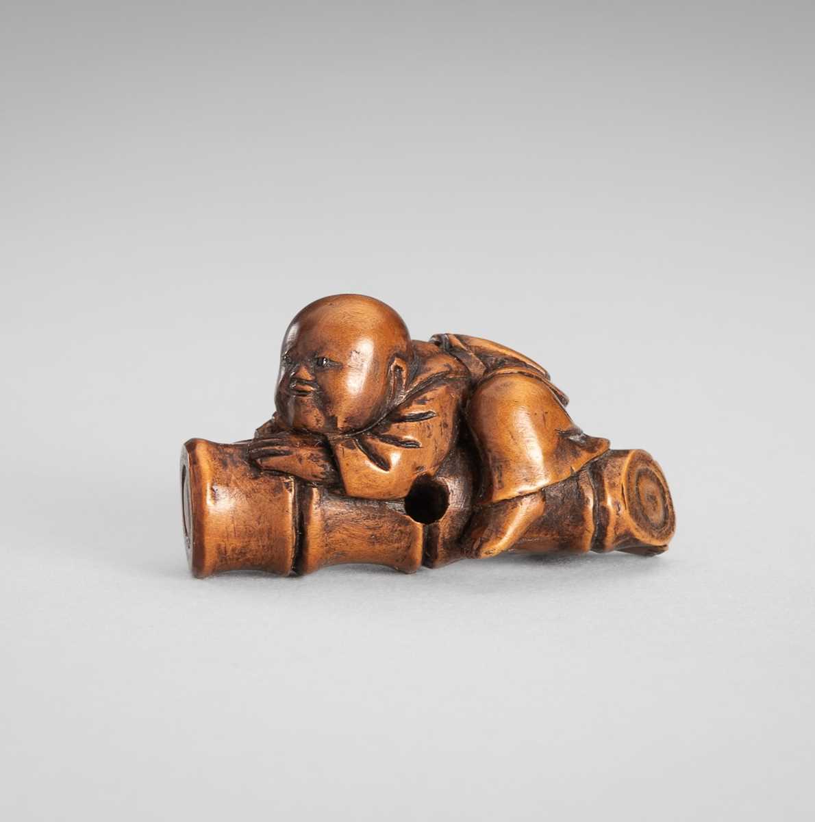Lot 349 - A WOOD NETSUKE OF A BOY ON A BAMBOO LOG