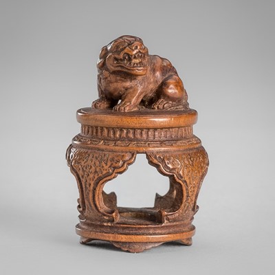 Lot 1604 - TOMOCHIKA: A FINE WOOD NETSUKE OF A SHISHI ON A TABLE