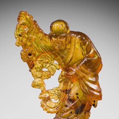 Lot 118 - A TRANSLUCENT AMBER CARVING OF XIANGLONG LUOHAN, QING DYNASTY