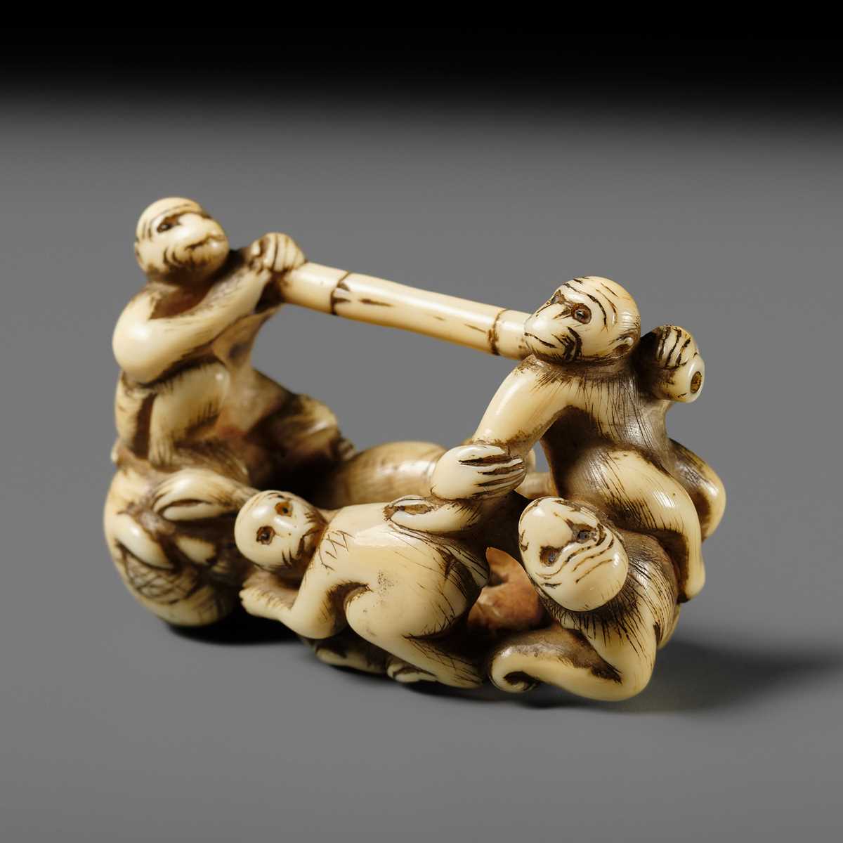 AN AMUSING IVORY NETSUKE OF A GROUP OF MONKEYS CARRYING A BAMBOO POLE