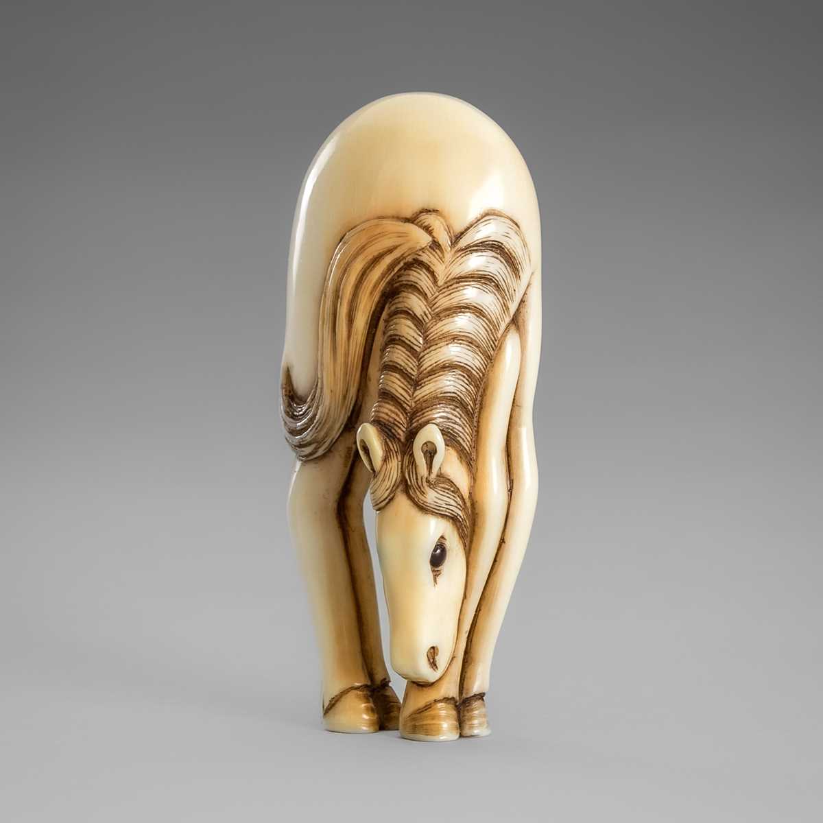 Lot 499 - AN IVORY NETSUKE OF A GRAZING HORSE