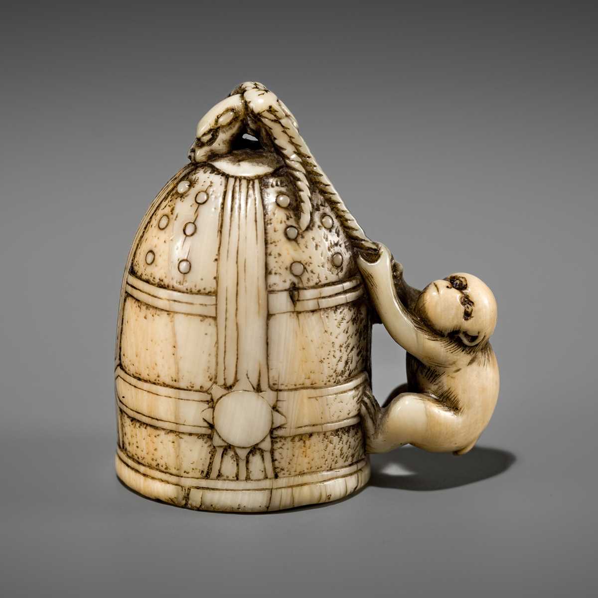 Lot 124 - A FINE KYOTO SCHOOL IVORY NETSUKE OF A MONKEY SCALING A TEMPLE BELL (BONSHO)