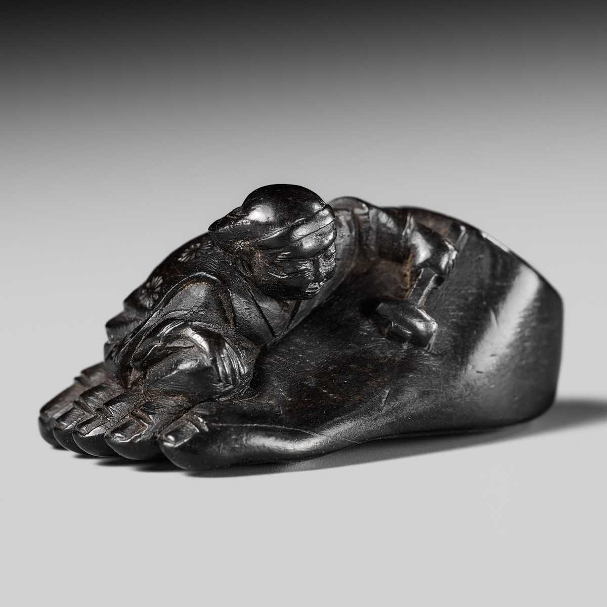 Lot 417 - HOSHUNSAI MASAYUKI: A RARE EBONY WOOD NETSUKE OF A CARVER CHISELING A GIANT FOOT