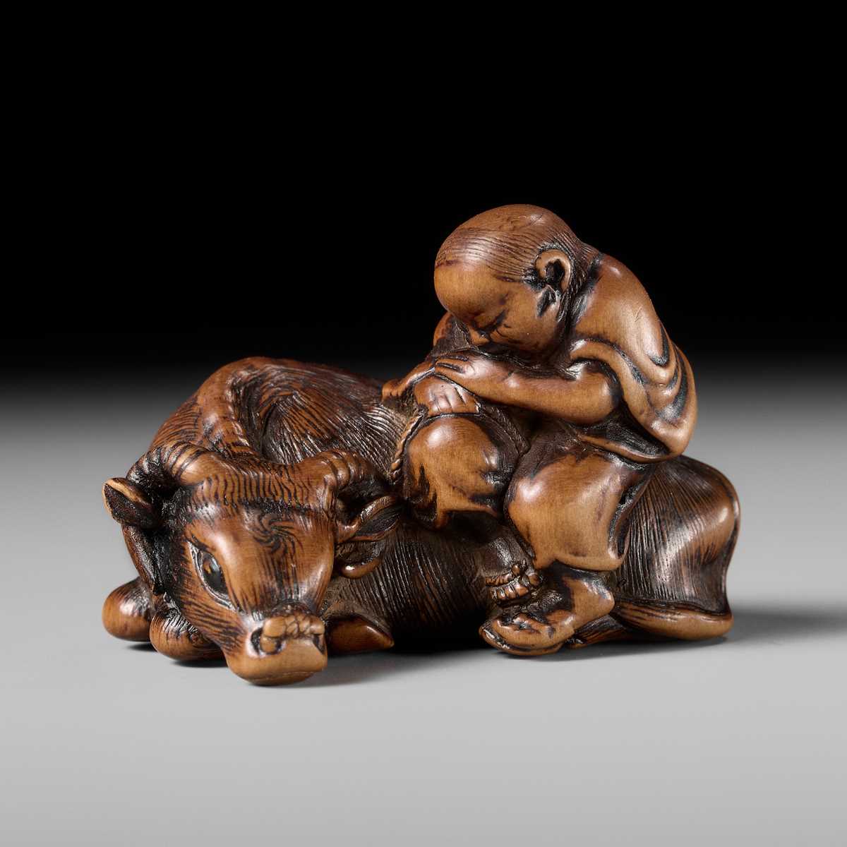 A FINE WOOD NETSUKE OF A HERDBOY SLEEPING ON AN OX
