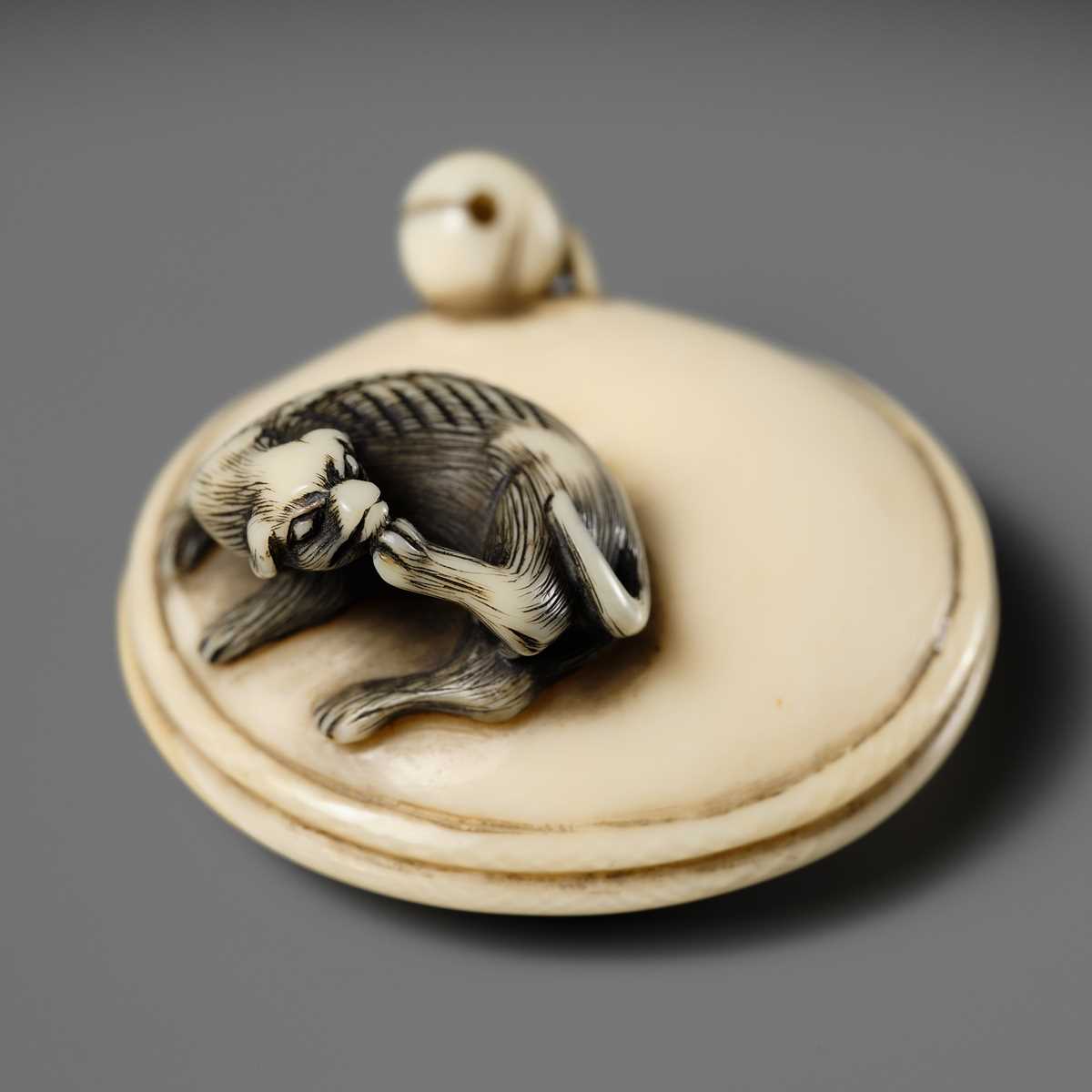 MITSUHARU: AN IVORY NETSUKE OF A DOG ON A CUSHION