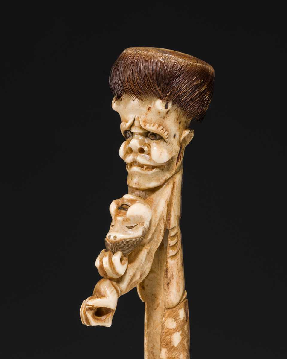 Lot 76 - AN ANTLER KISERUZUTSU (PIPE CASE) OF AN ONI WITH AN OKAME MASK