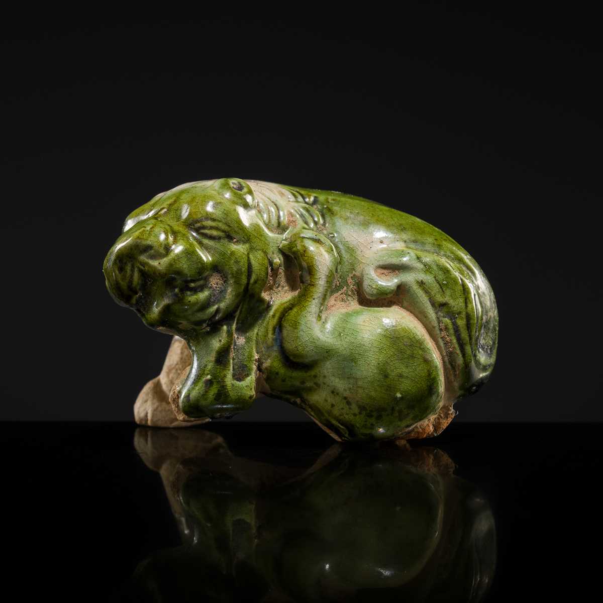 Lot 43 - A GREEN AND WHITE GLAZED POTTERY FIGURE OF A LION SCRATCHING ITSELF, TANG DYNASTY