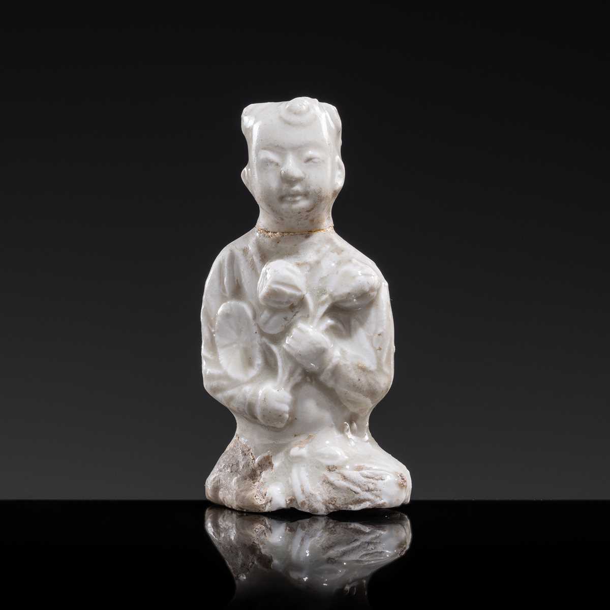 A SMALL WHITE GLAZED DINGYAO FIGURE OF A SEATED BOY WITH LOTUS FLOWERS, NORTHERN SONG DYNASTY