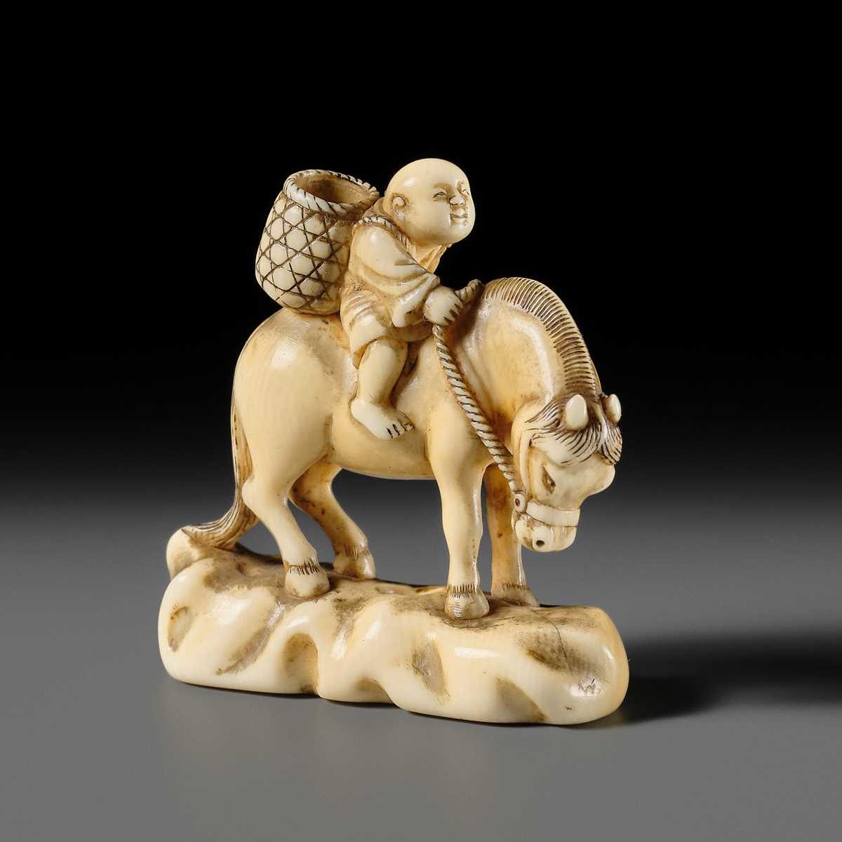 Lot 86 - AN IVORY NETSUKE OF A BOY ON A HORSE