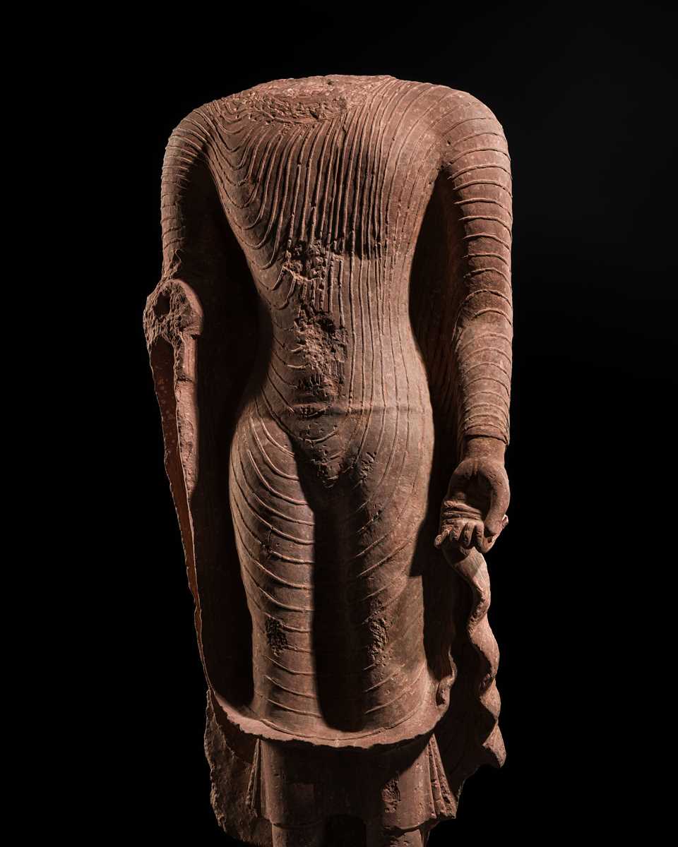 AN ICONIC RED SANDSTONE TORSO OF THE BUDDHA, GUPTA PERIOD, MATHURA, 3RD-5TH CENTURY