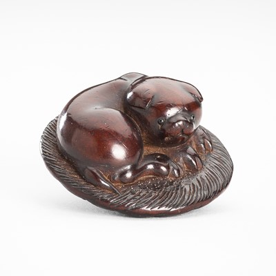 Lot 1547 - TOSHU: A CHARMING WOOD NETSUKE OF A PUPPY ON A STRAW MAT