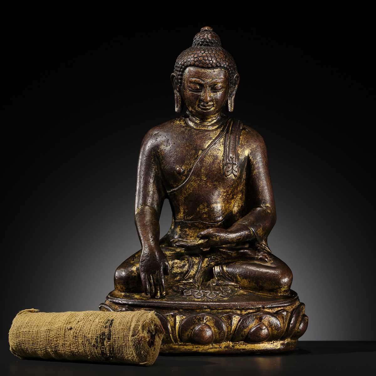 Lot 12 - AN INCSCRIBED GILT-COPPER FIGURE OF BUDDHA SHAKYAMUNI, NEPAL, LATE 13TH-EARLY 14TH CENTURY