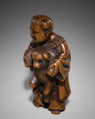 A CHARMING WOOD NETSUKE DEPICTING A KARAKO BOY HOLDING A PUPPY