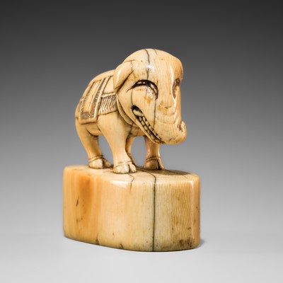 Lot 424 - AN UNUSUAL AND CHARMING IVORY SEAL NETSUKE OF A GRINNING, CAPARISONED ELEPHANT