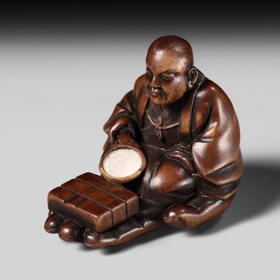 RYUKEI: A RARE WOOD NETSUKE OF A MAN SEATED ON THE HAND OF BUDDHA