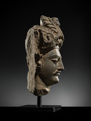 Lot 248 - A LARGE SCHIST HEAD OF A BODHISATTVA WITH A ‘KĪRTIMUKHA’ TURBAN, GANDHARA, 4TH–5TH CENTURY, FORMERLY IN THE COLLECTION OF BEGUM BAKHT ZEBA