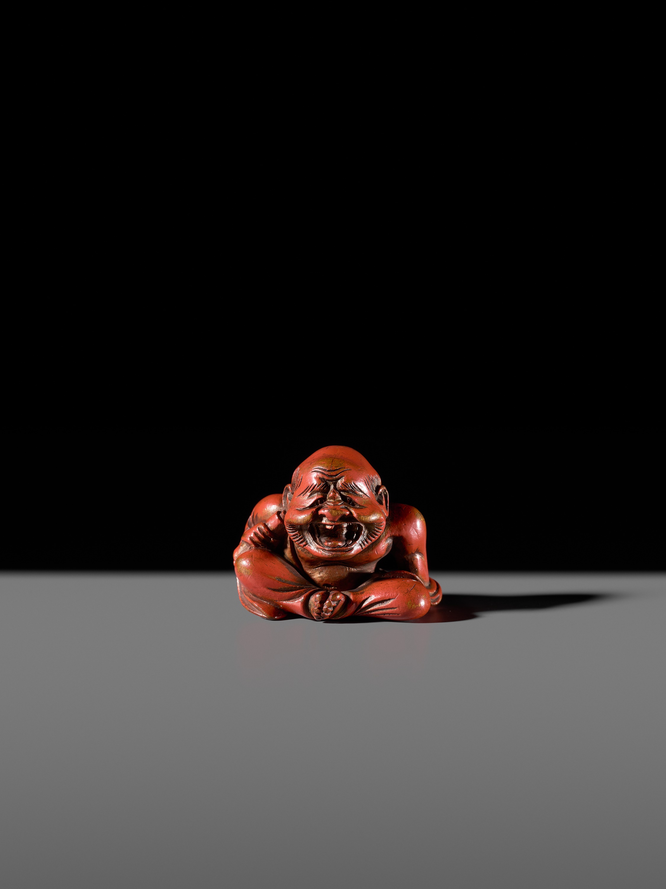 Lot 65 - A RARE RED LACQUER NETSUKE OF A LAUGHING