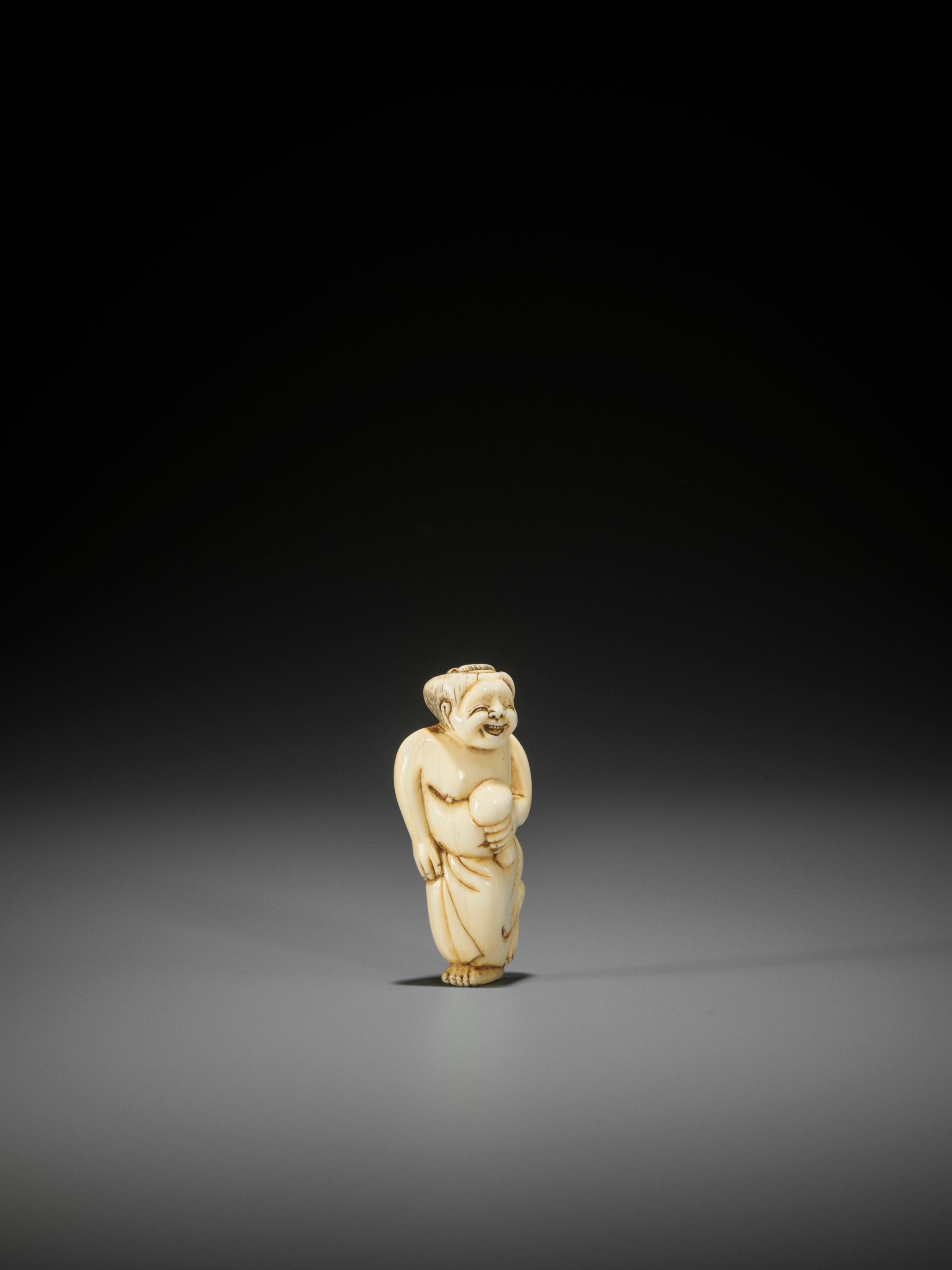 Lot 27 - AN IVORY SHUNGA NETSUKE OF OKAME HOLDING A