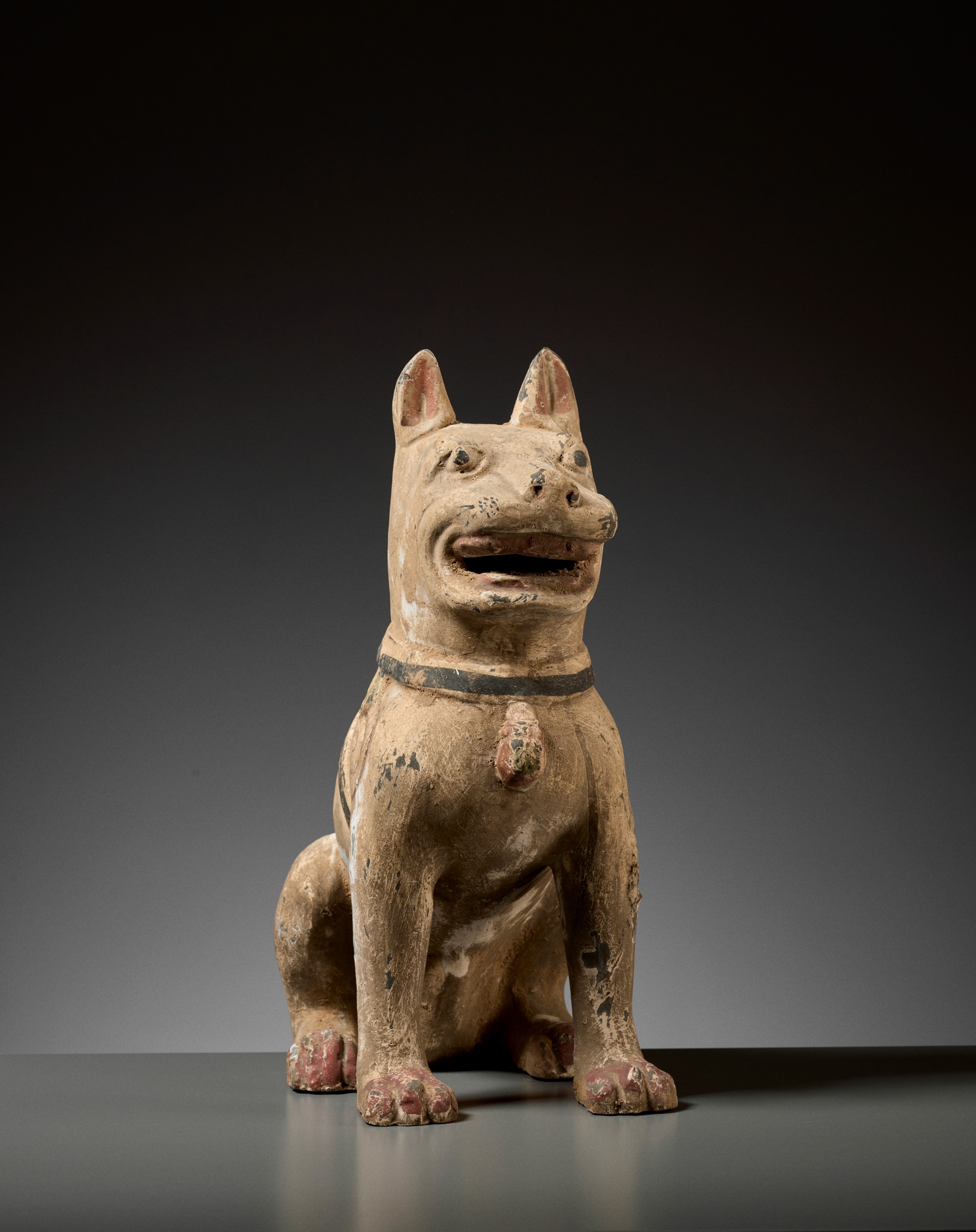 Lot 140 - A PAINTED GRAY POTTERY FIGURE OF A GUARD DOG,